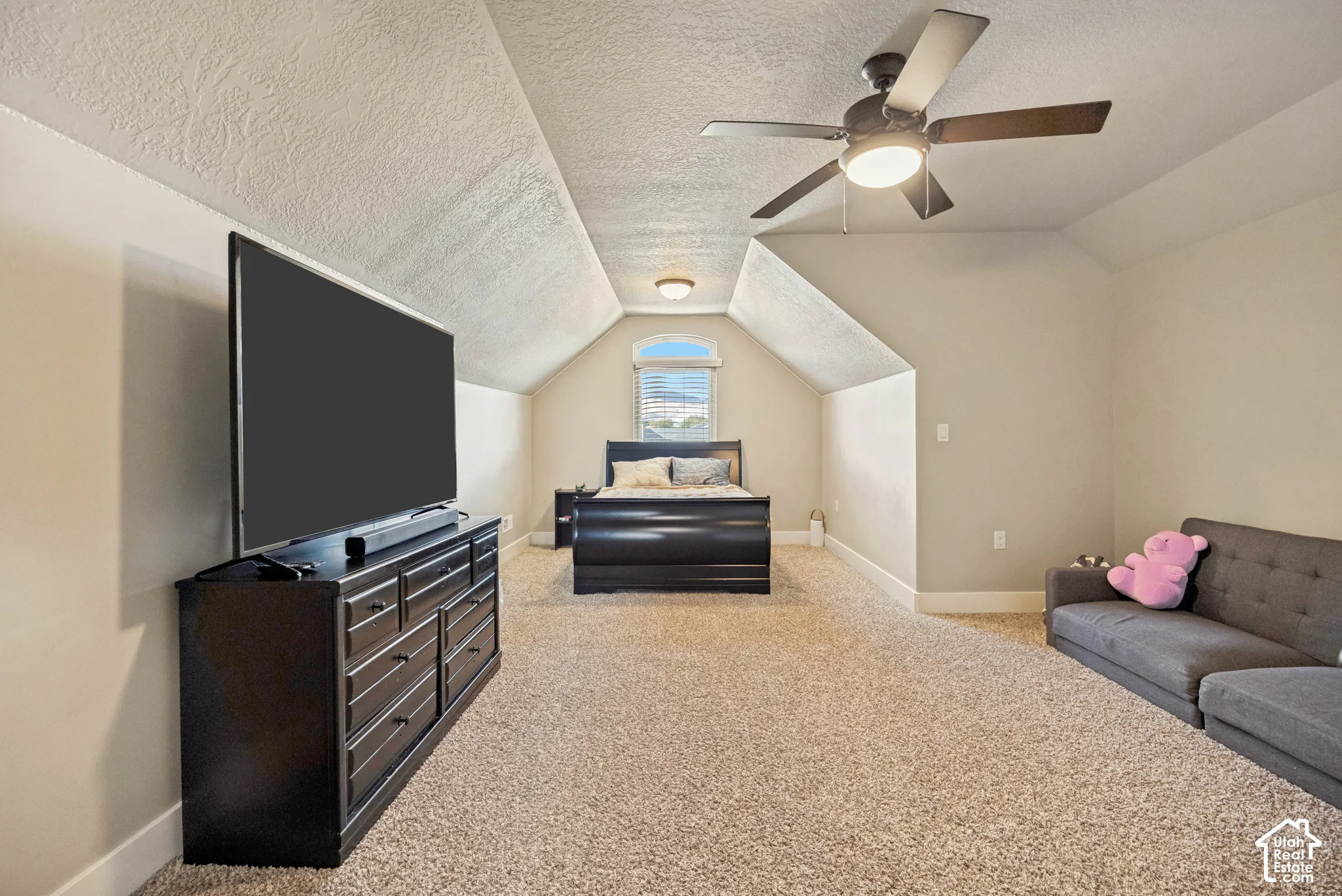 Vaulted ceilings featuring a central arched window, neutral wall-to-wall carpeting, and a multi-blade ceiling fan