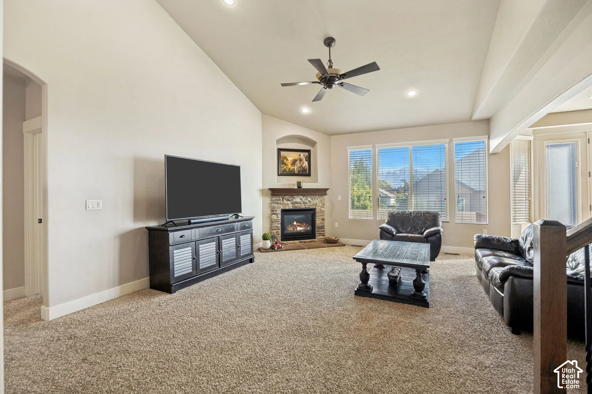 Vaulted ceilings, fireplace with stone surround, recessed lighting, ceiling fan, and large windows