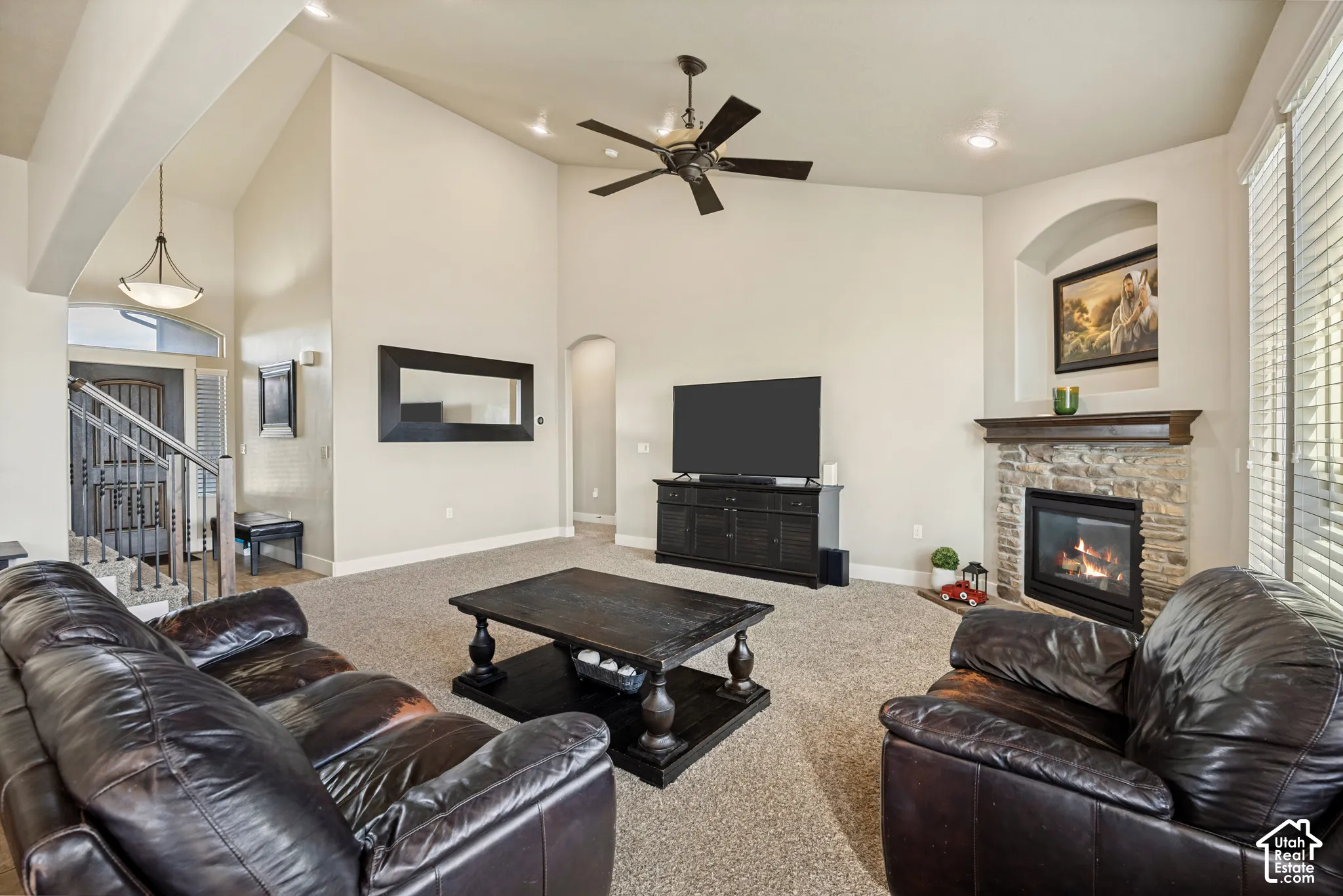 Vaulted ceilings, stone fireplace with a wood mantel, arched wall niche, recessed lighting, and a ceiling fan