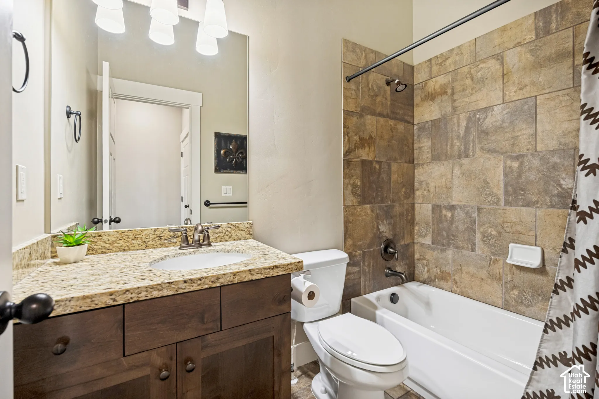 Bathroom featuring a wood-finish vanity with a stone countertop, under-mount sink, tile-surround shower combination, and oil-rubbed bronze fixtures