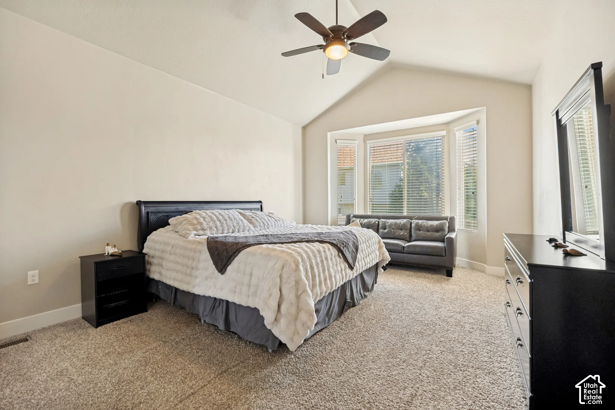 Vaulted ceilings featuring a central overhead fan, neutral wall finishes, carpeted flooring, and a multi-paneled bay window