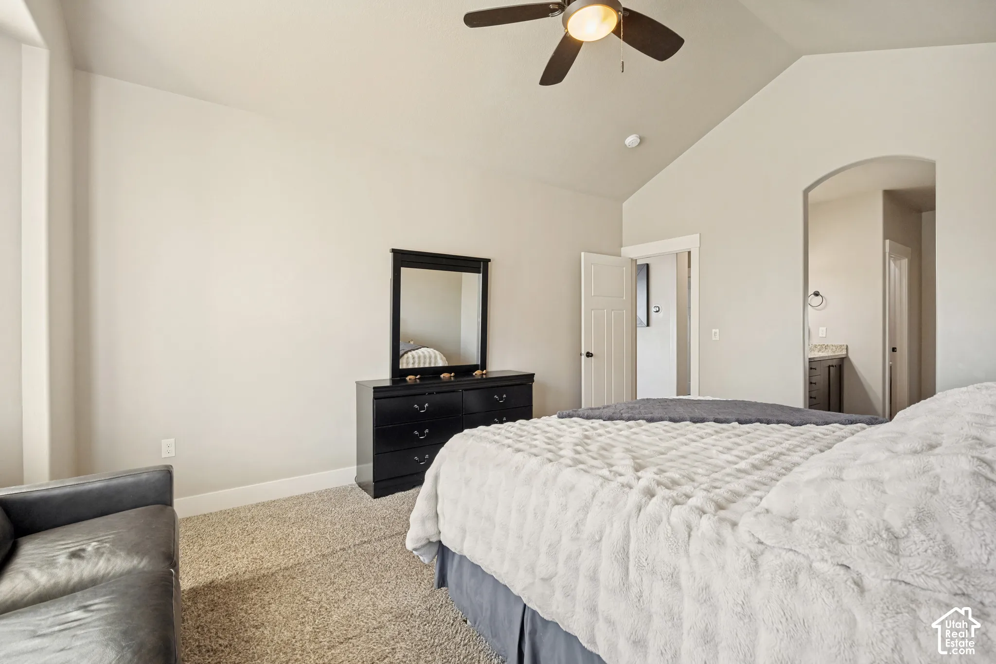 Vaulted ceilings with a central ceiling fan, neutral wall finishes, carpeted flooring, and an arched entryway