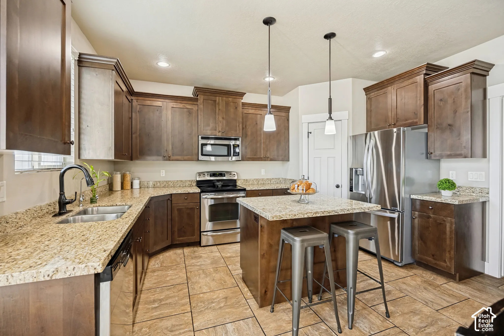 Kitchen featuring stained wood cabinetry, stone countertops, stainless steel appliances, a central island, and tile flooring
