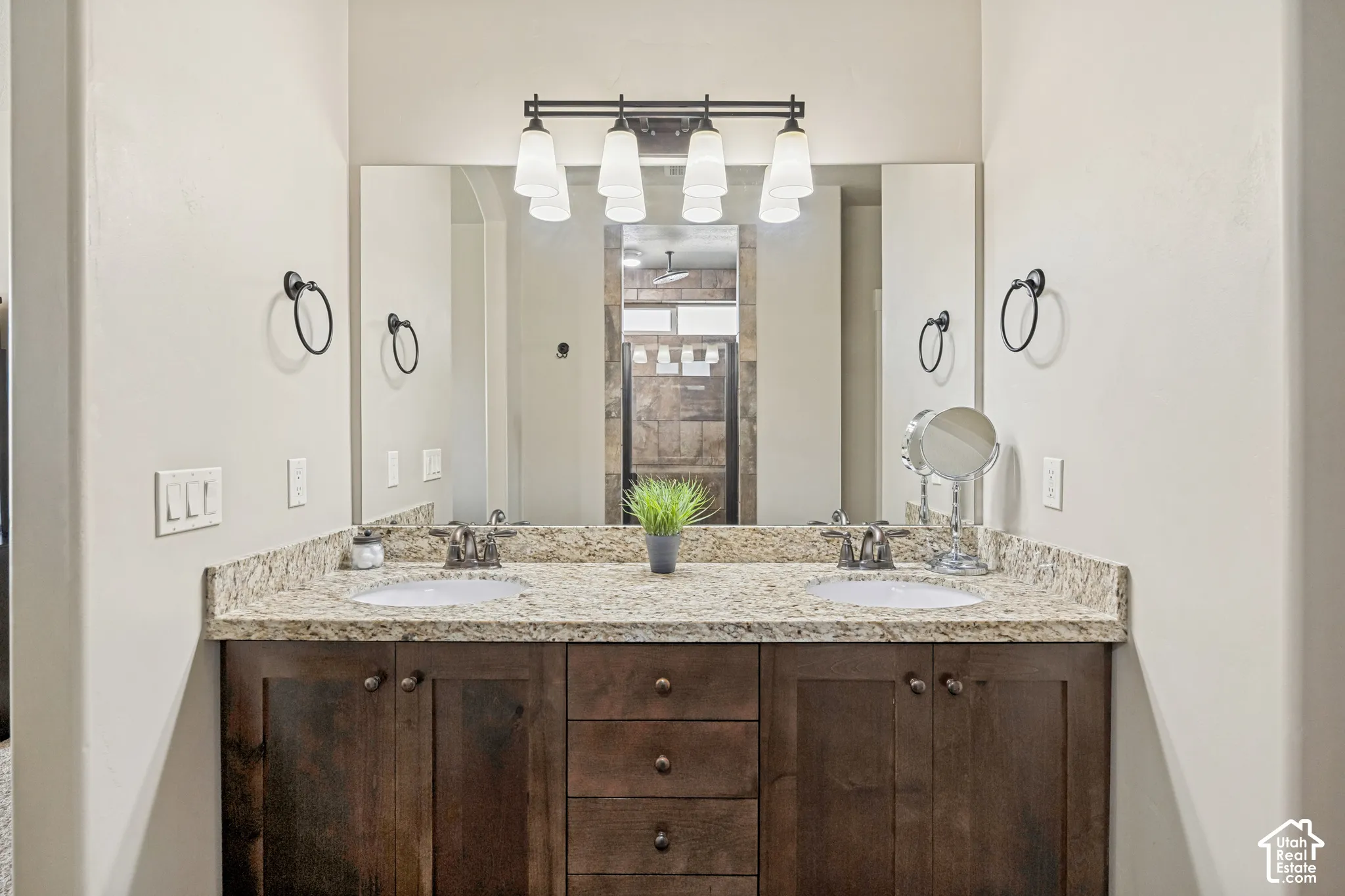 Dual-sink vanity with stone-finish countertop, dark wood-finish cabinetry, full-width wall mirror, and four-light fixture