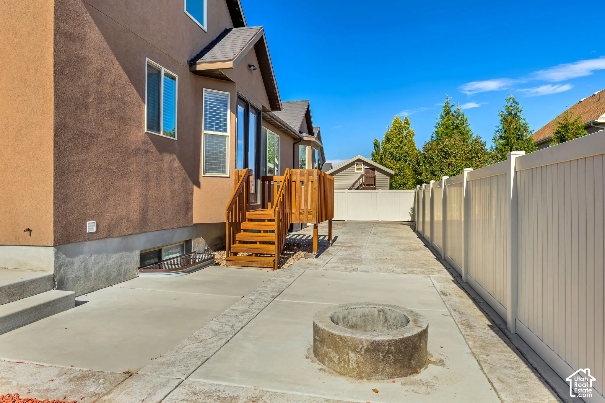 Stucco exterior home featuring a wood-construction deck, concrete patio, built-in concrete fire pit, and full-perimeter vinyl privacy fencing