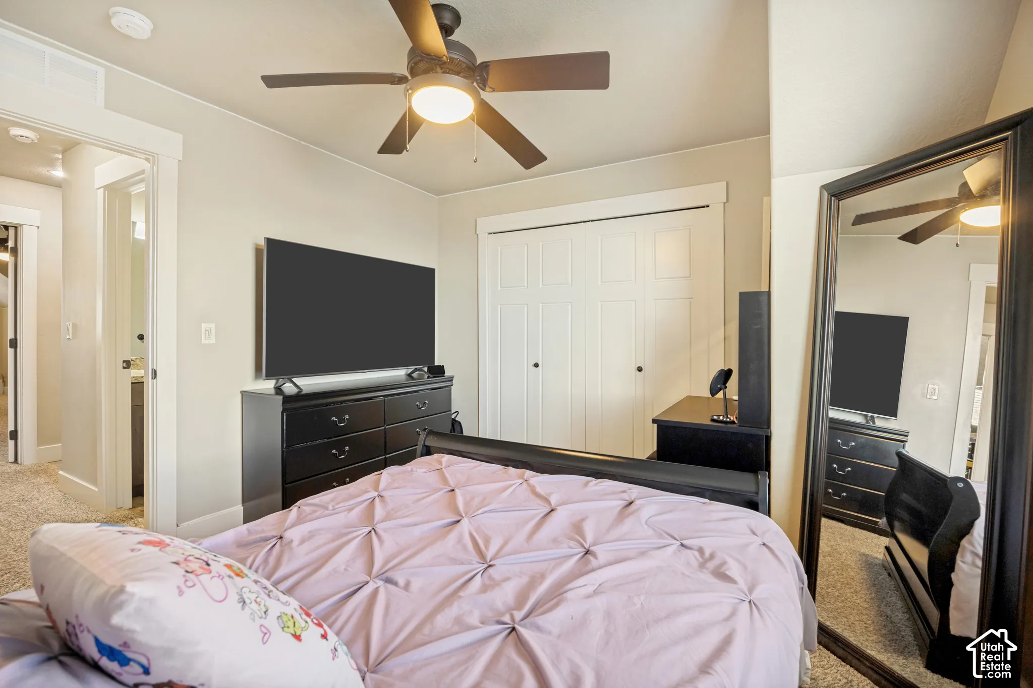 Neutral-toned walls with crisp white door and window casing, textured carpeting, double-door closet with clean trim, and a ceiling-mounted light fixture with an integrated fan
