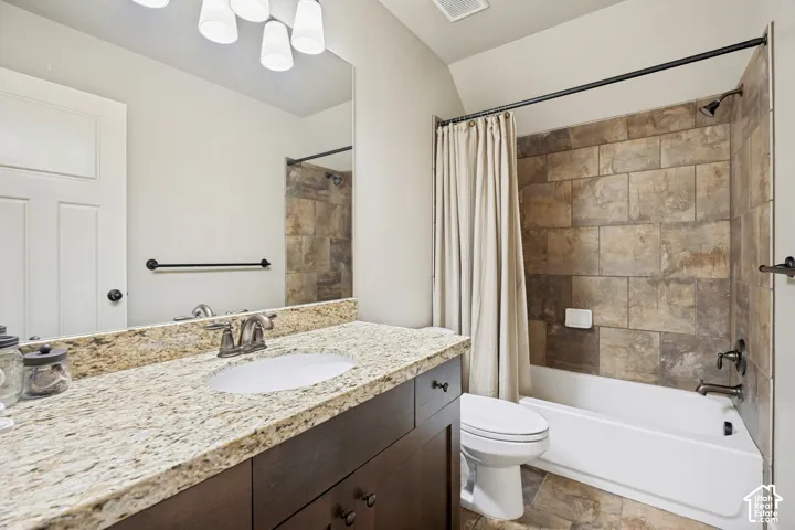 Bathroom featuring dark wood-finish cabinetry, stone-patterned countertop, under-mount sink, tile tub surround, and tile flooring