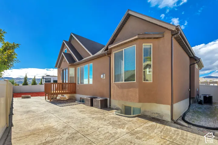 Stucco exterior featuring multiple roof gables, a raised wood deck, a stamped concrete patio, and a mountain backdrop