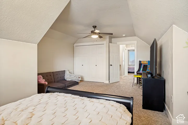 Vaulted ceiling featuring a ceiling fan with integrated lighting, wall-to-wall carpeting, and a dual-panel closet door
