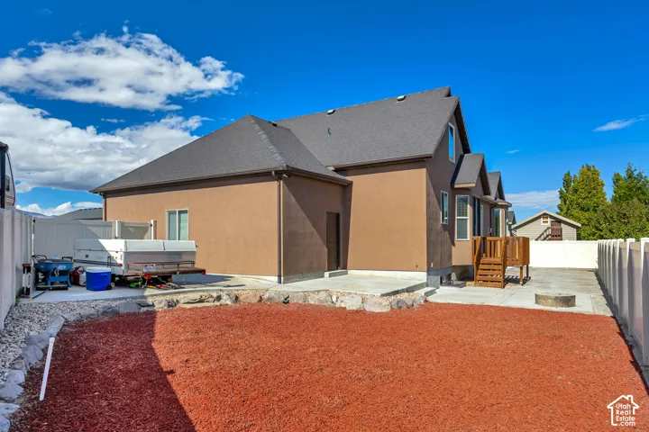 Exterior featuring a brown stucco finish, asphalt shingle roof, concrete patio, wood deck, and perimeter vinyl fencing