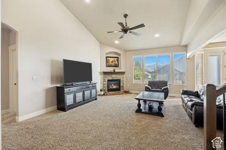 Vaulted ceilings, fireplace with stone surround, recessed lighting, ceiling fan, and large windows