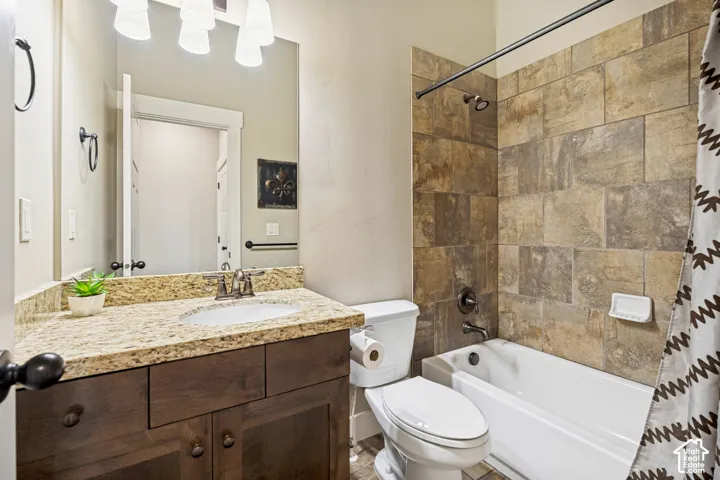 Bathroom featuring a wood-finish vanity with a stone countertop, under-mount sink, tile-surround shower combination, and oil-rubbed bronze fixtures
