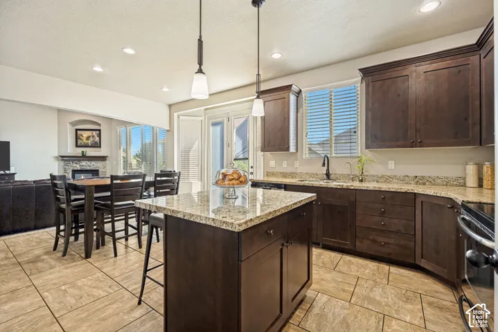 Kitchen featuring dark wood cabinetry, stone countertops, a center island, tile flooring, and dual pendant lighting