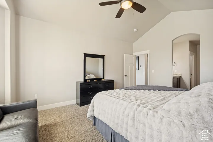 Vaulted ceilings with a central ceiling fan, neutral wall finishes, carpeted flooring, and an arched entryway