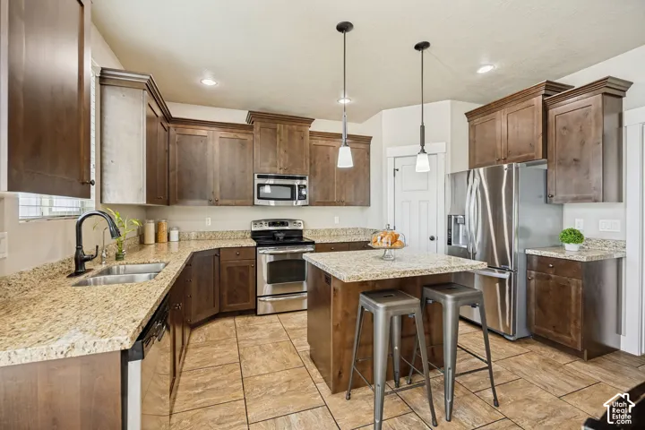 Kitchen featuring stained wood cabinetry, stone countertops, stainless steel appliances, a central island, and tile flooring