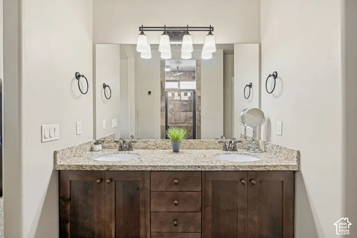 Dual-sink vanity with stone-finish countertop, dark wood-finish cabinetry, full-width wall mirror, and four-light fixture