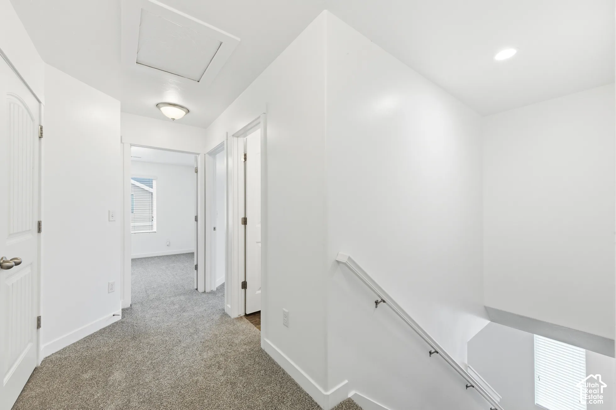 Interior hallway featuring neutral carpeting, recessed ceiling lighting, multi-panel doors, and a staircase with a white handrail