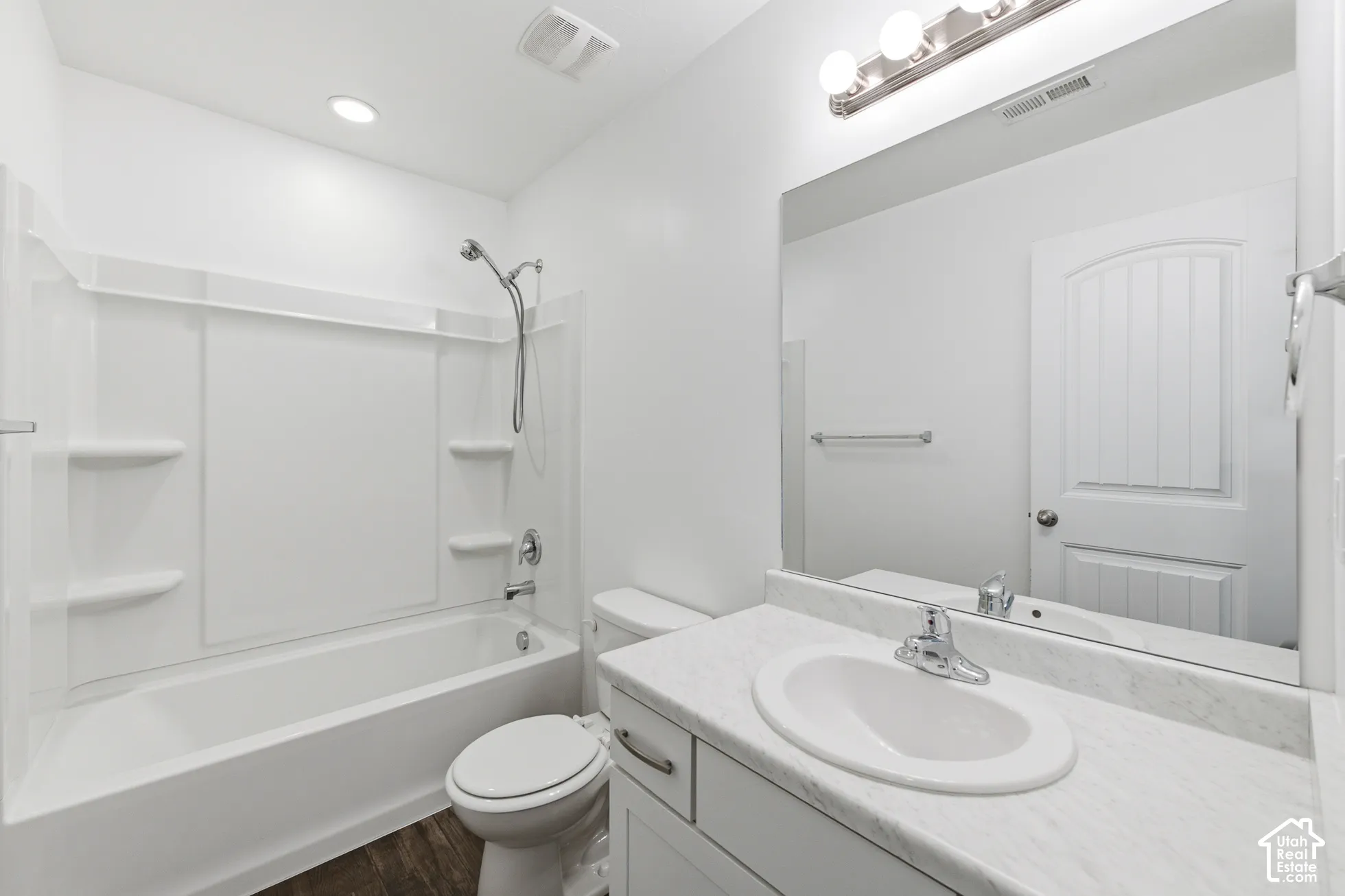 Bathroom featuring white cabinetry, stone-finish countertop with integrated oval sink, full-width mirror, and shower-tub combination with integrated shelving