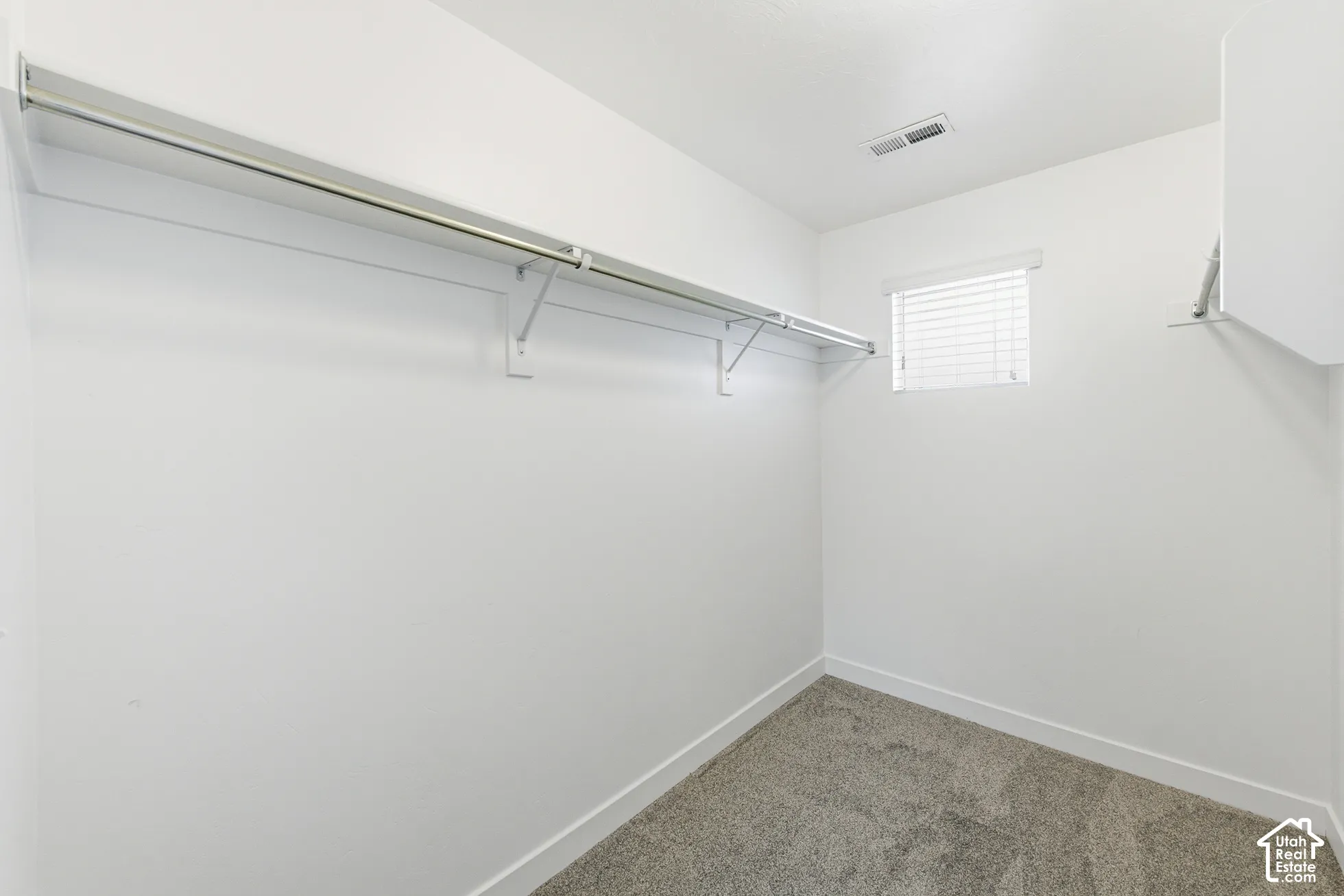 Walk-in closet featuring neutral carpeting, white walls, and built-in metal shelving rods with horizontal blinds