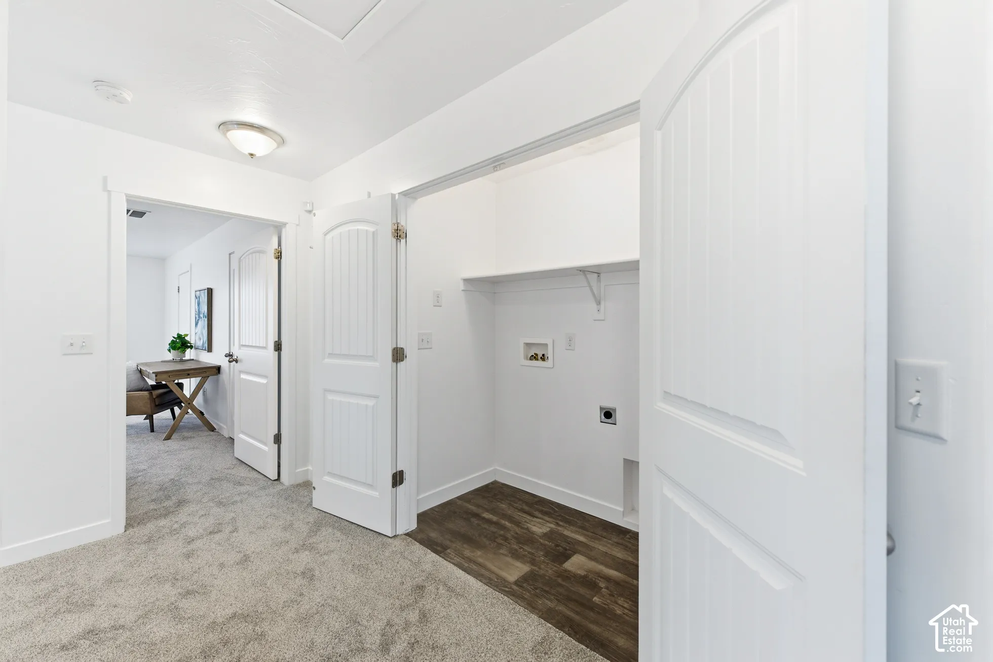 Laundry alcove featuring wood-finish flooring, built-in shelving, and hookups for laundry appliances, framed by a multi-panel door