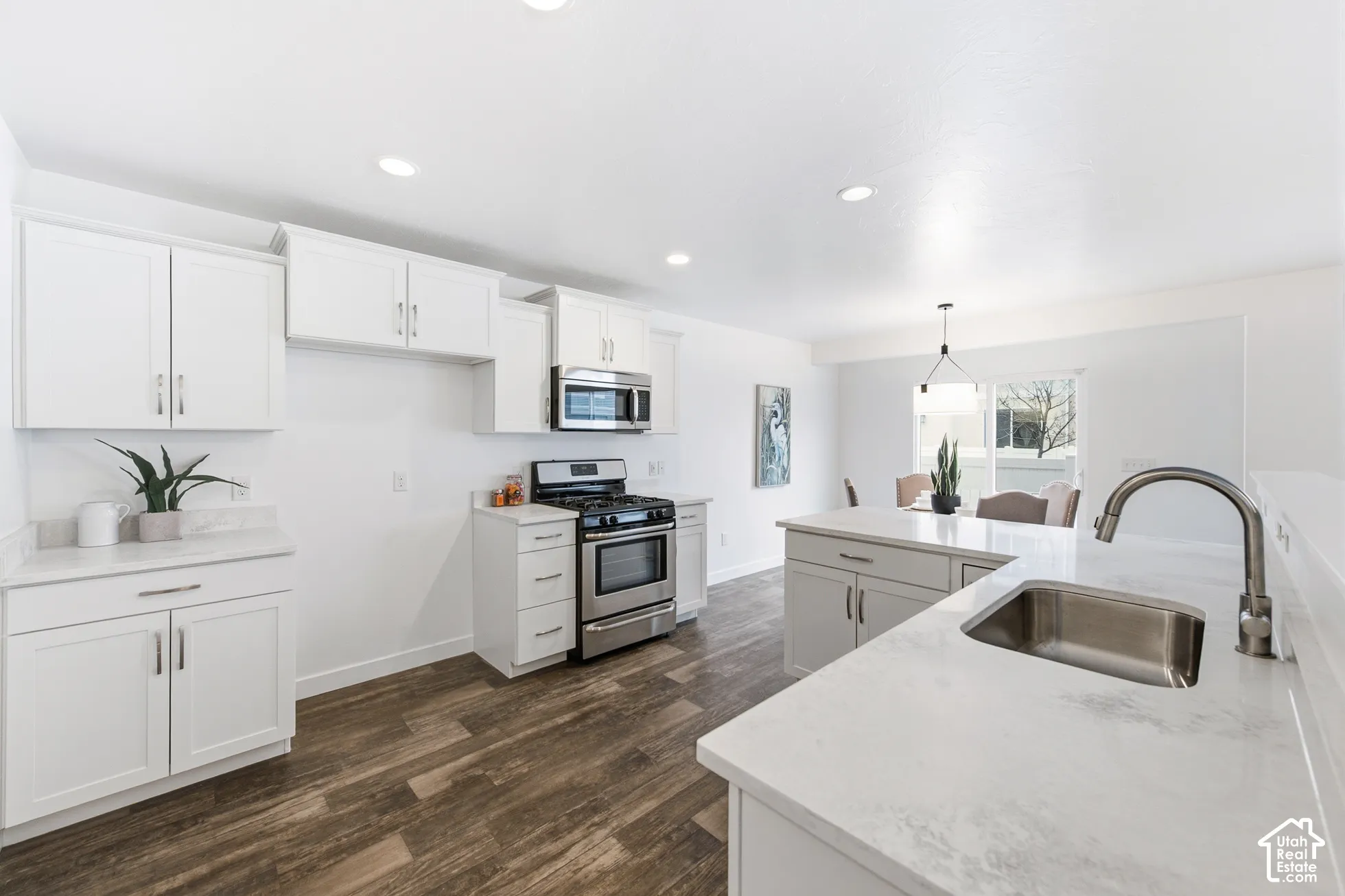 Kitchen featuring white shaker-style cabinetry, solid-surface countertops, wood-finish flooring, stainless steel appliances, and an undermount sink with a gooseneck faucet