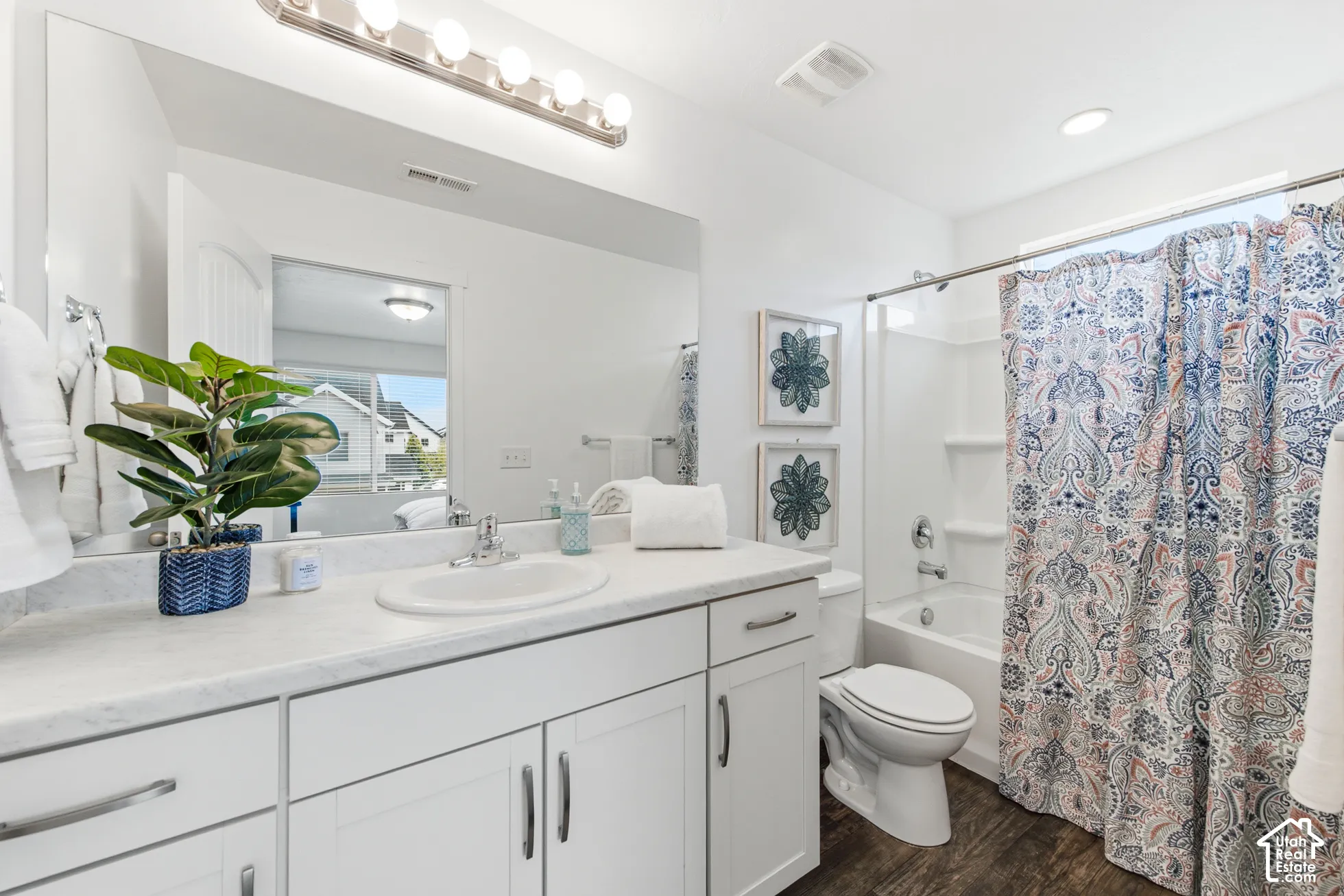 Bathroom featuring white cabinetry, solid-surface countertop with an integrated oval sink, wood-finish flooring, and a tub-shower combination with a surround