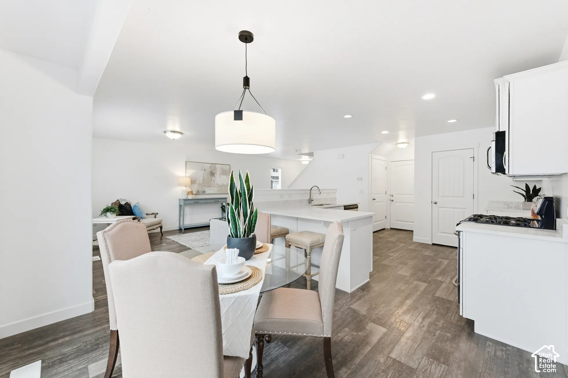 Open concept interior featuring wood-finish flooring, white shaker-style cabinetry, stone-surfaced island with sink, and recessed ceiling lighting
