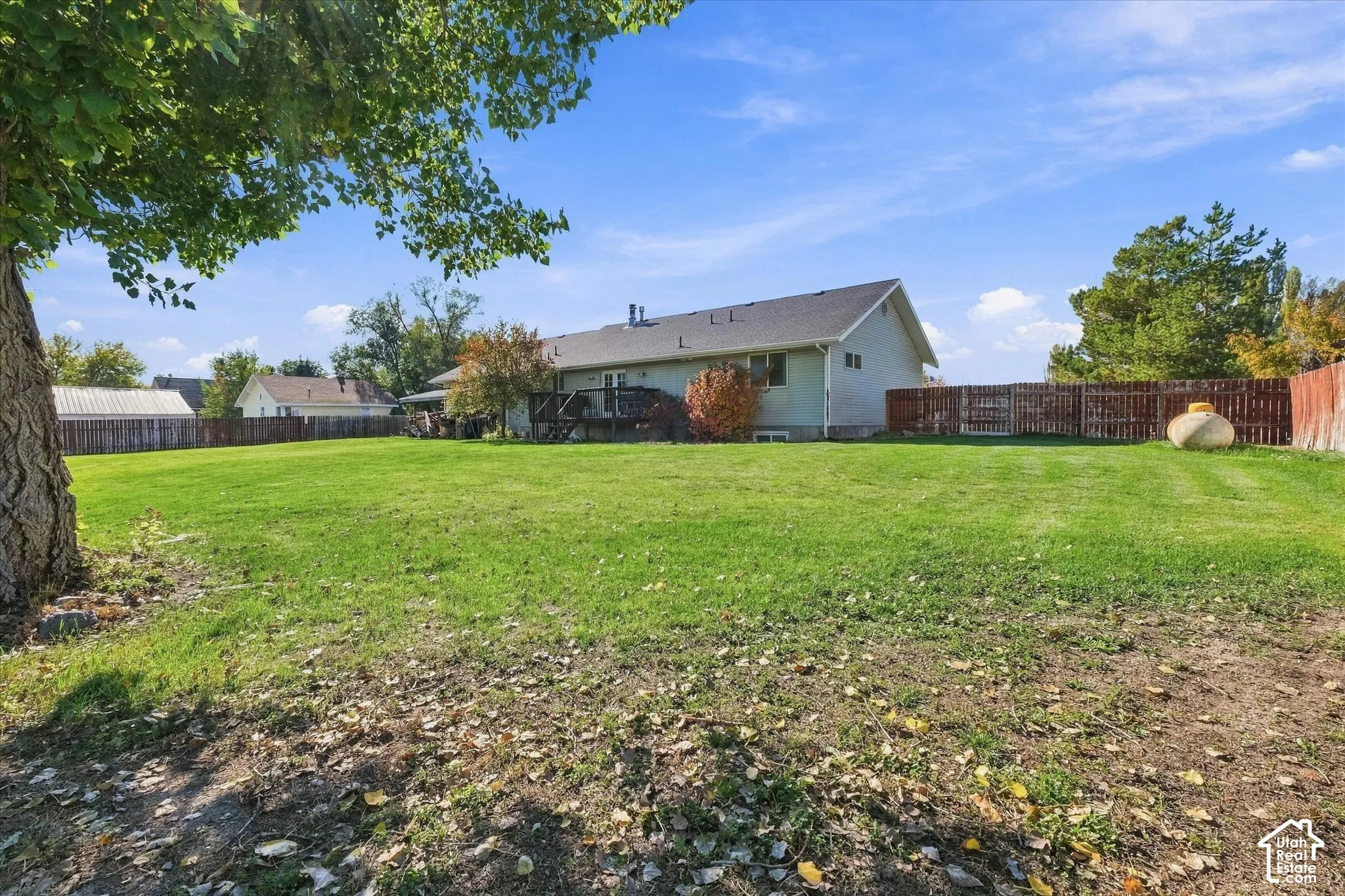 Expansive backyard featuring a large grass lawn, perimeter wood fencing, and an elevated wooden deck