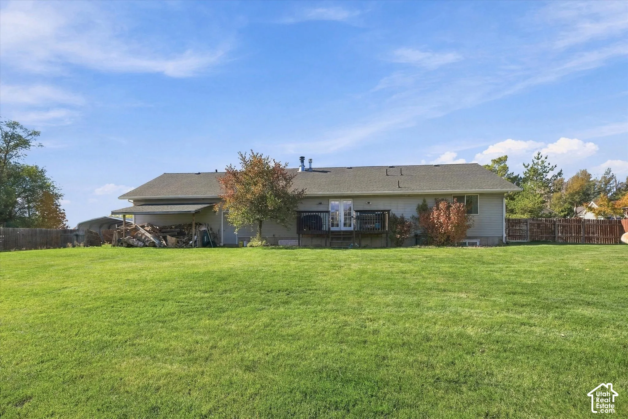 Expansive backyard featuring a large grass lawn, a wood deck, a covered outdoor storage area, and perimeter wood fencing