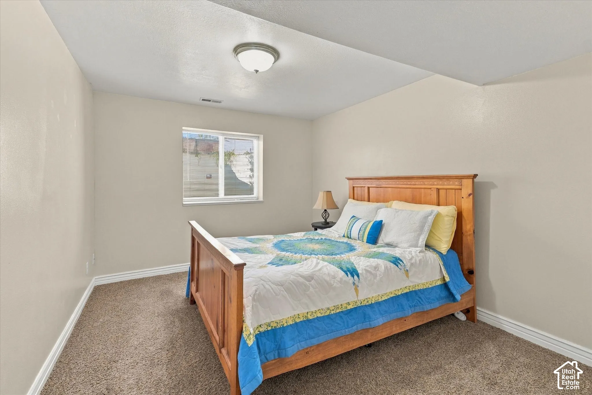 Neutral-toned interior featuring wall-to-wall carpeting, a sliding window with a window well, and a flush-mount ceiling light fixture