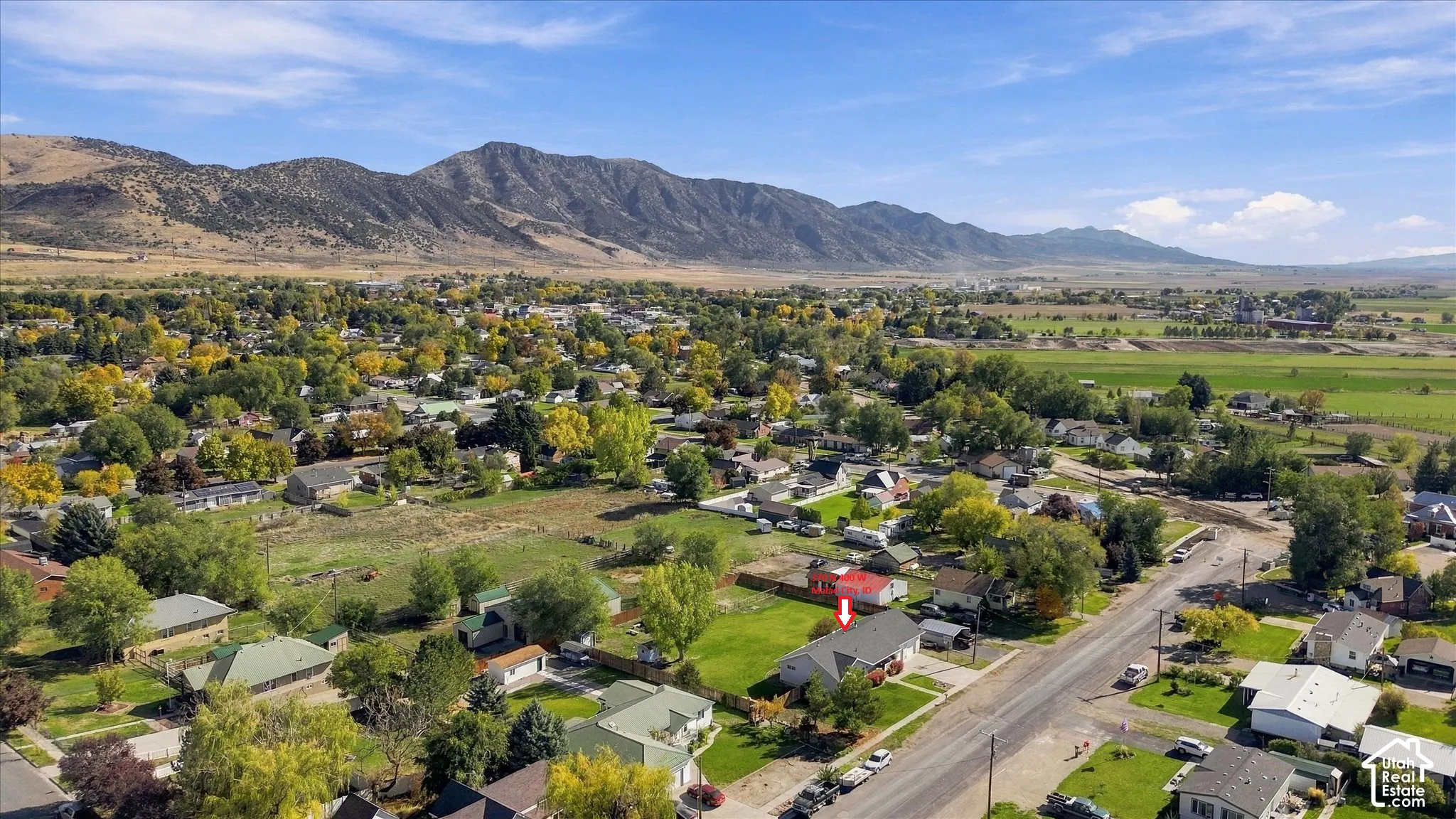 Aerial perspective of a residential lot featuring a multi-slope roof, expansive open lawn area, mature trees, and prominent mountain backdrop