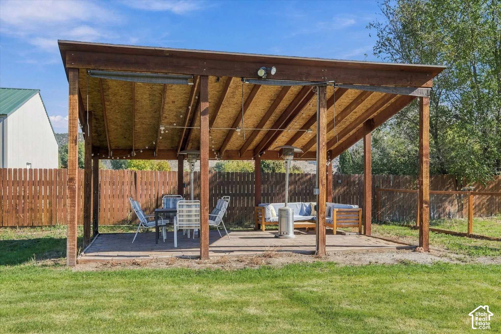 Covered outdoor patio featuring a timber-frame structure, exposed ceiling beams, concrete slab flooring, and perimeter wood privacy fencing