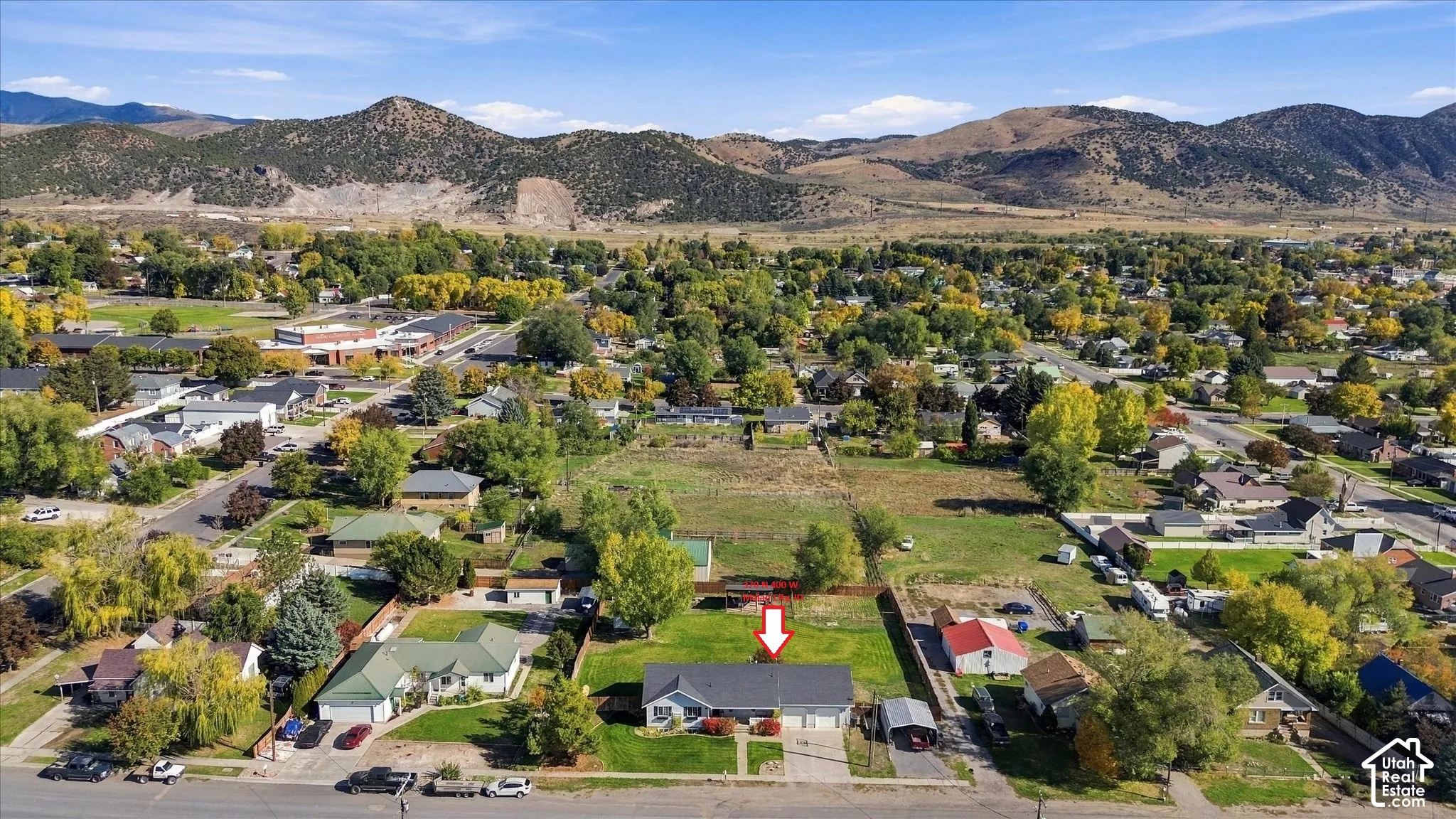 Aerial perspective featuring a single-story residence with an attached garage, situated on a lot with established trees and a mountain backdrop