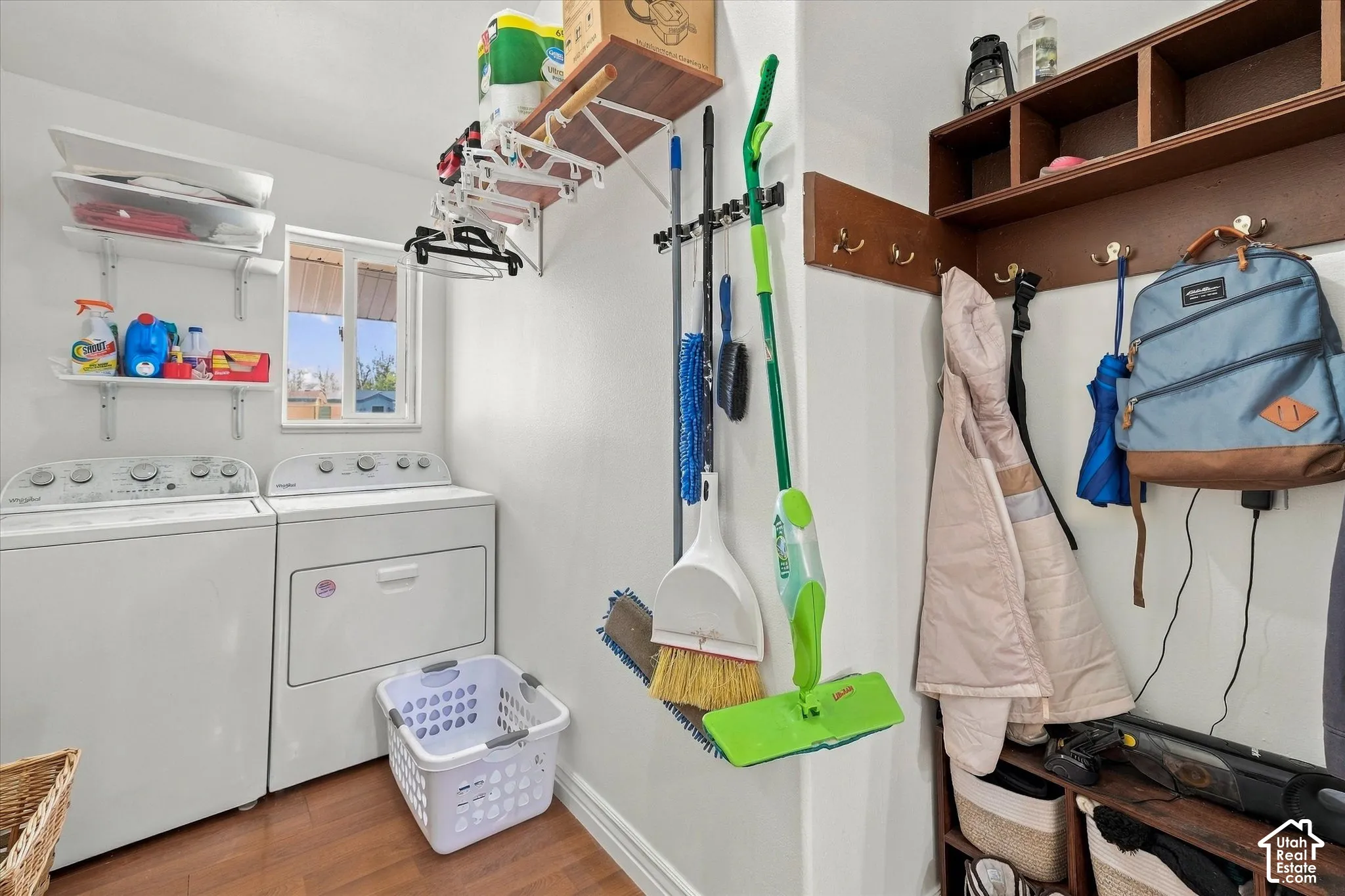 Laundry room featuring wood-finish flooring, white wall-mounted shelving, and built-in wood-finish storage cabinetry with metal hooks