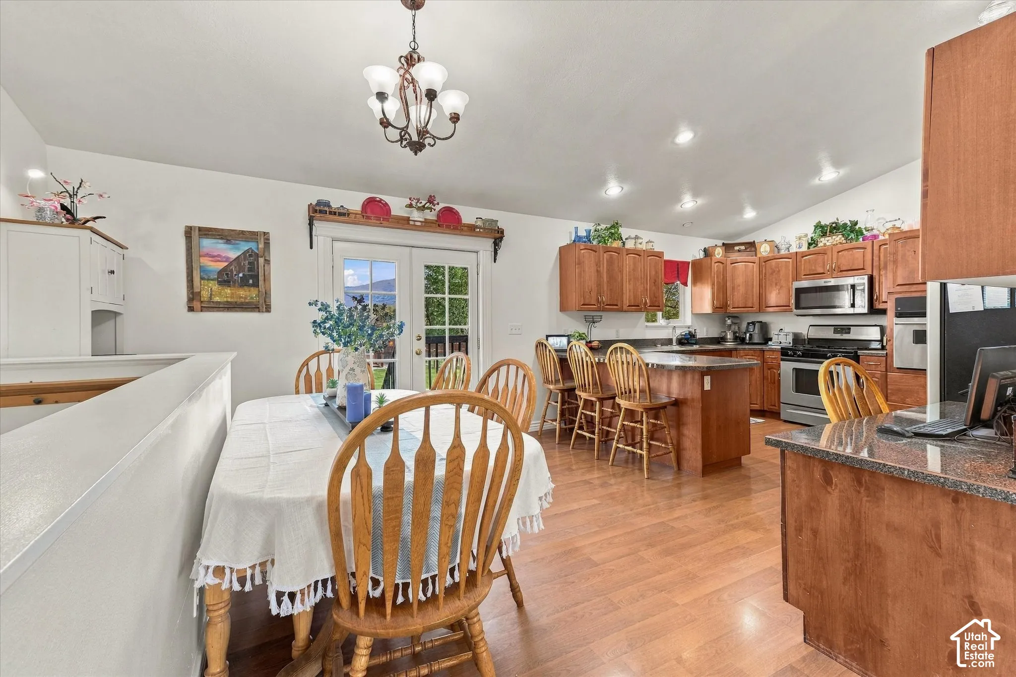 Kitchen featuring stained wood cabinetry, stainless steel appliances, wood-finish flooring, and a multi-light chandelier