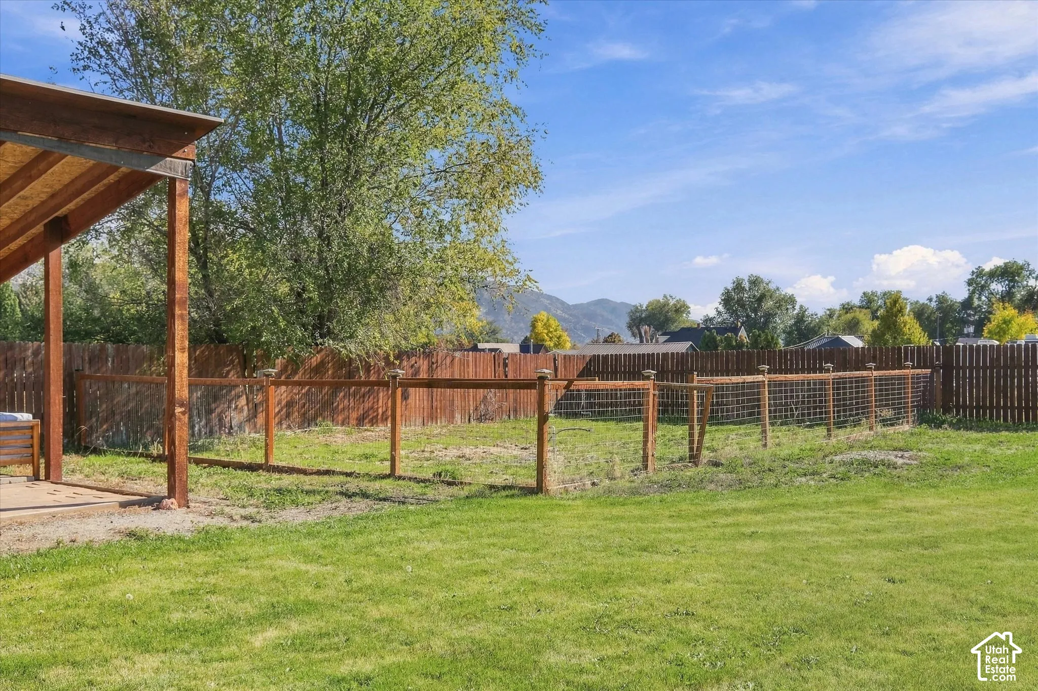 Expansive backyard featuring a covered patio, wood-post fencing, wire mesh enclosure, and mature trees