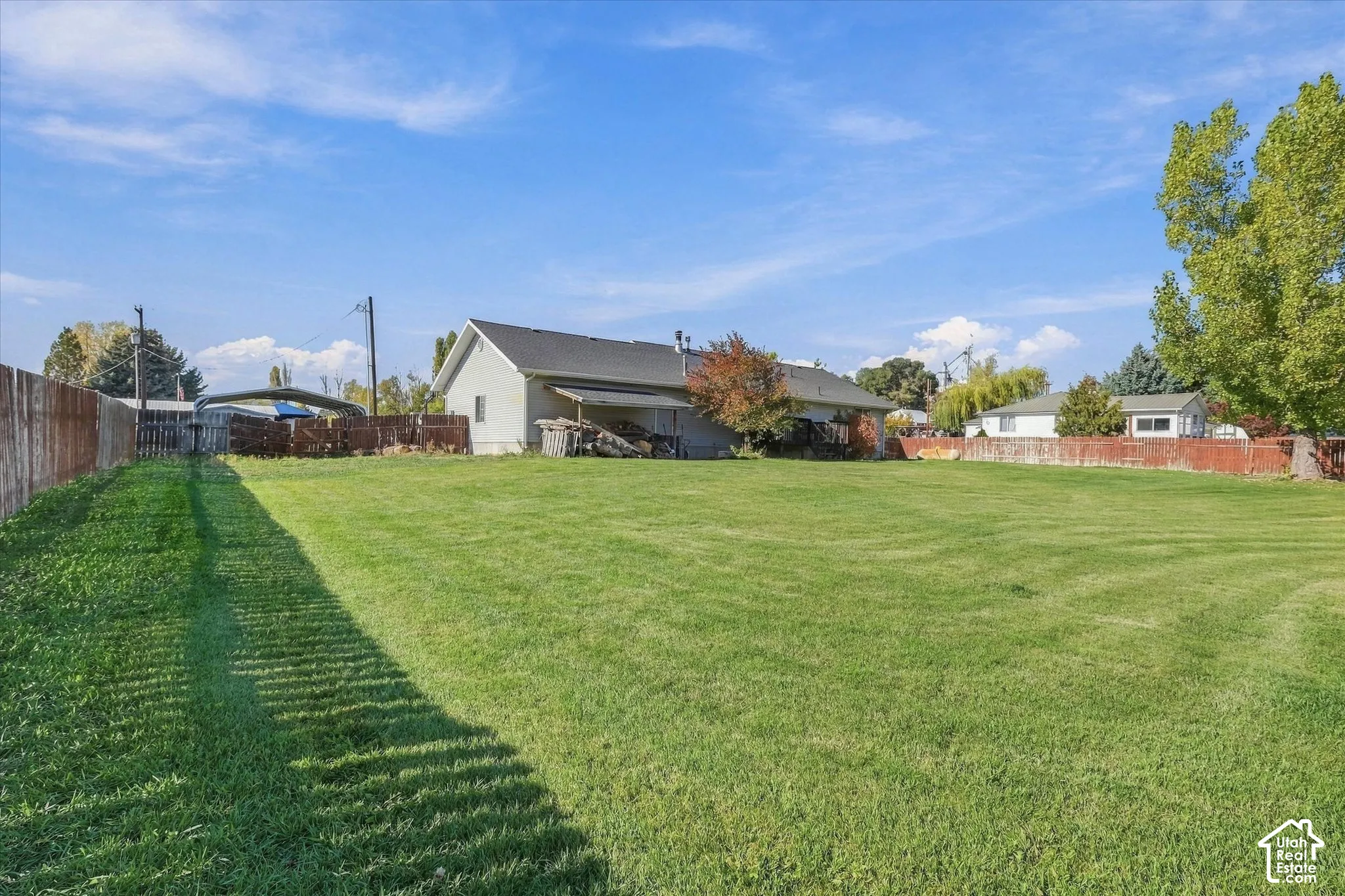 Expansive backyard featuring a large grass lawn, wood fencing, and mature trees