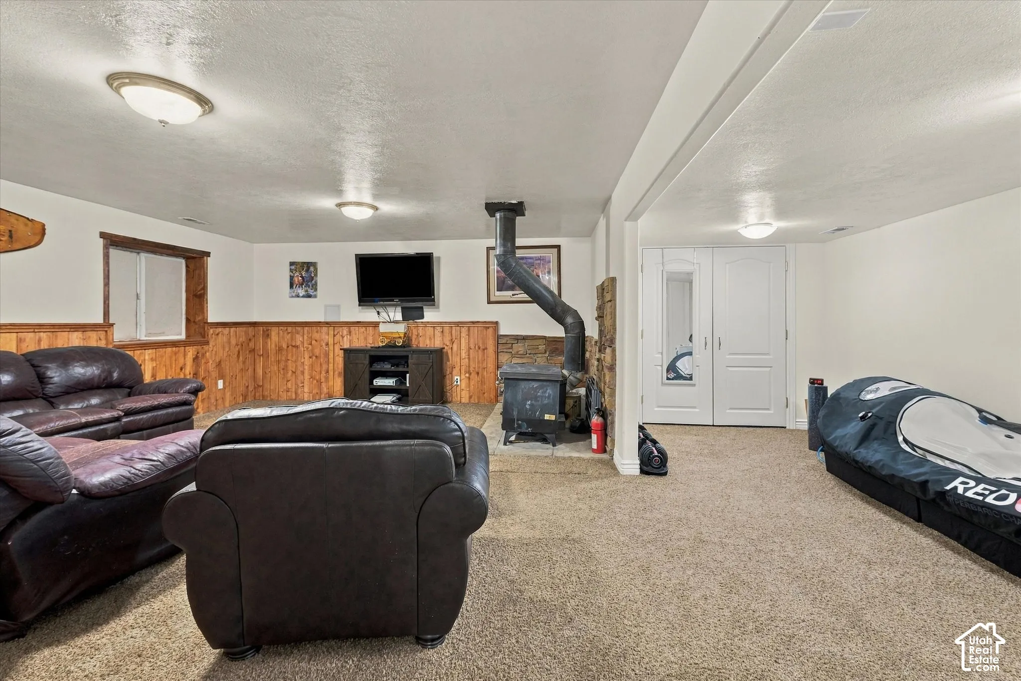 Interior space featuring wood-paneled wainscoting, a freestanding wood-burning stove with a stone hearth, neutral carpeting, and double-door storage cabinetry