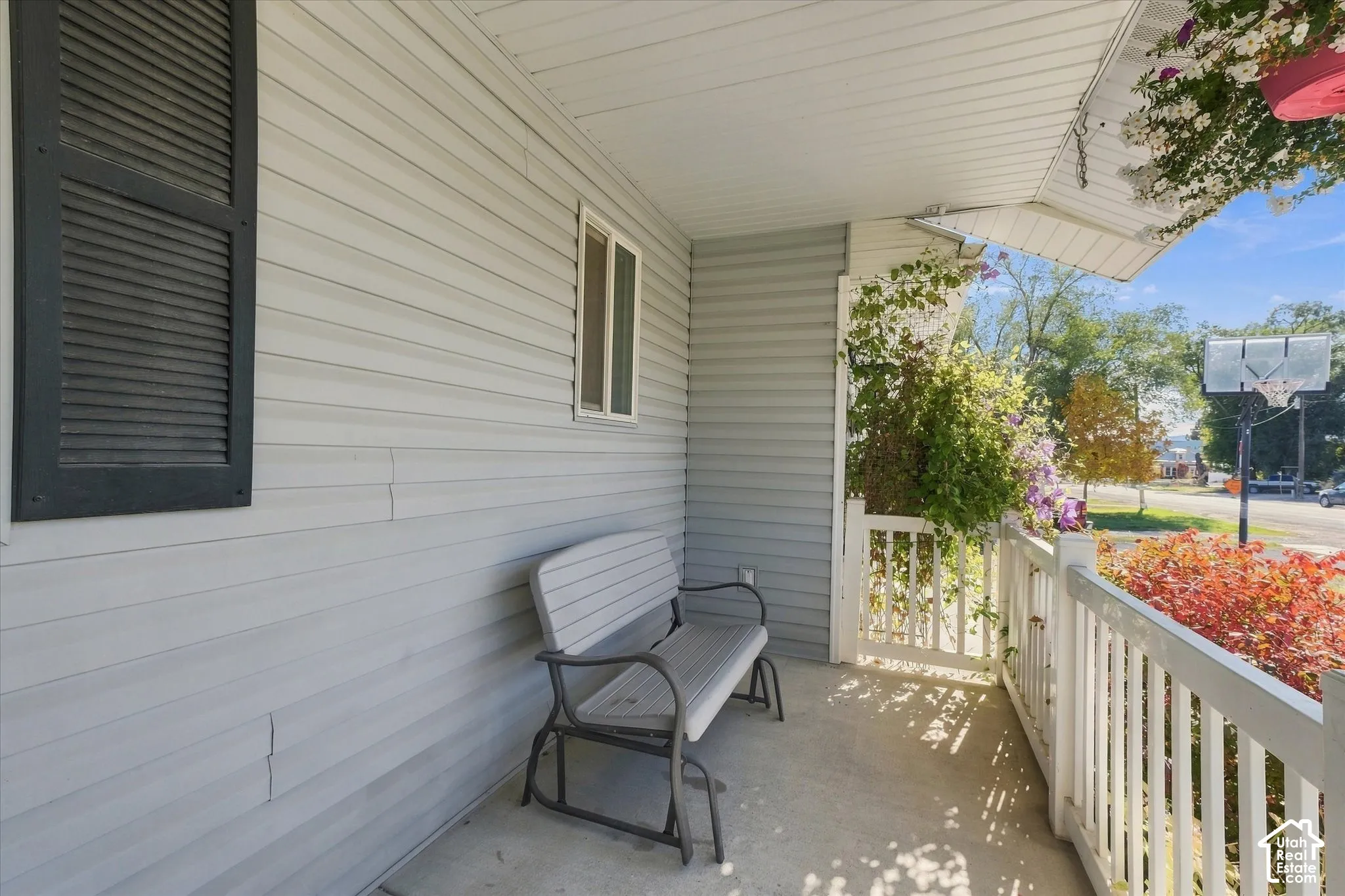 Covered front porch featuring light gray horizontal siding, vertical window shutters, and white painted railings