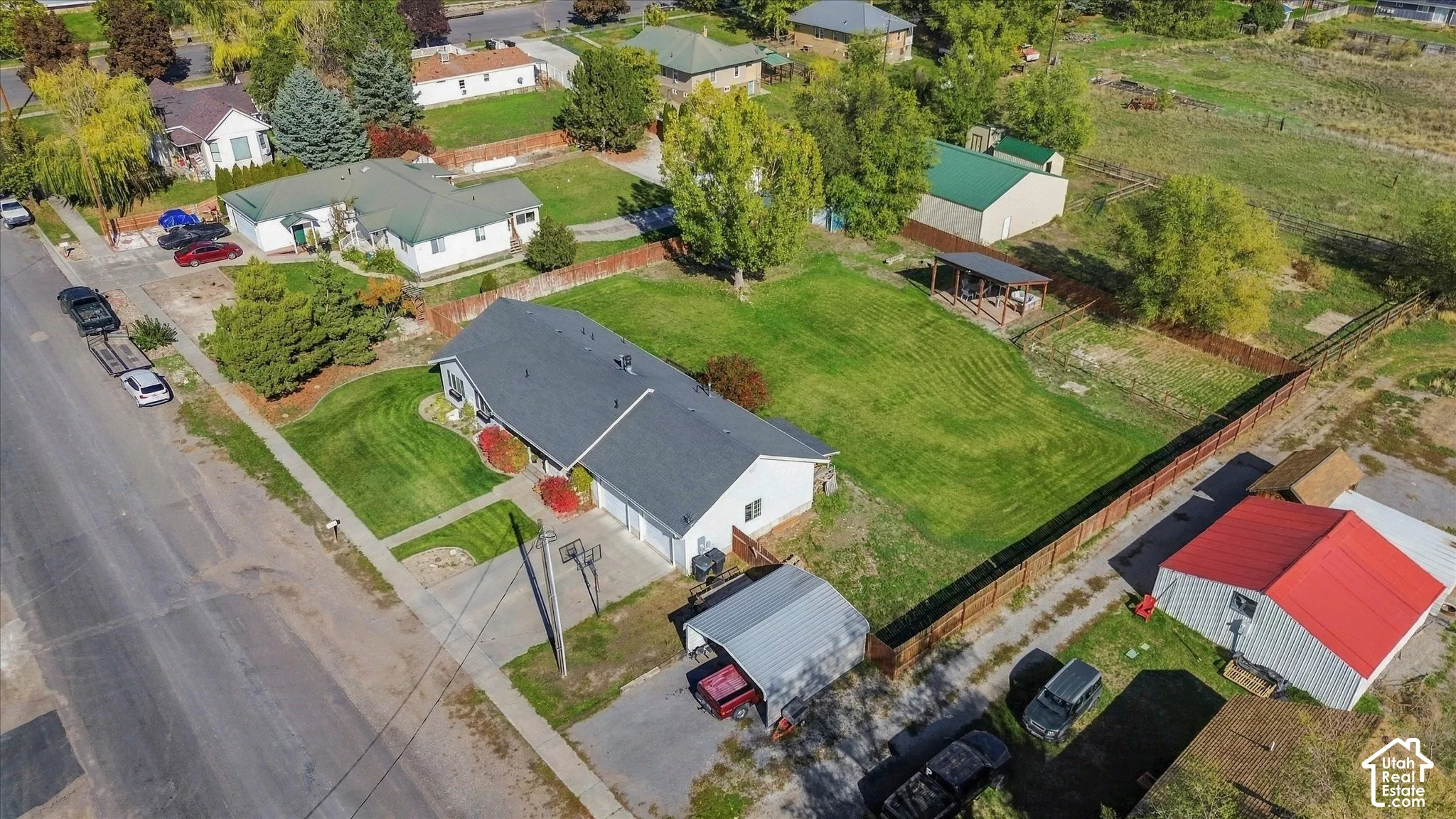 Aerial perspective featuring a sprawling lot with a grass lawn, metal-roofed detached workshop, covered carport, and wood-slat perimeter fencing