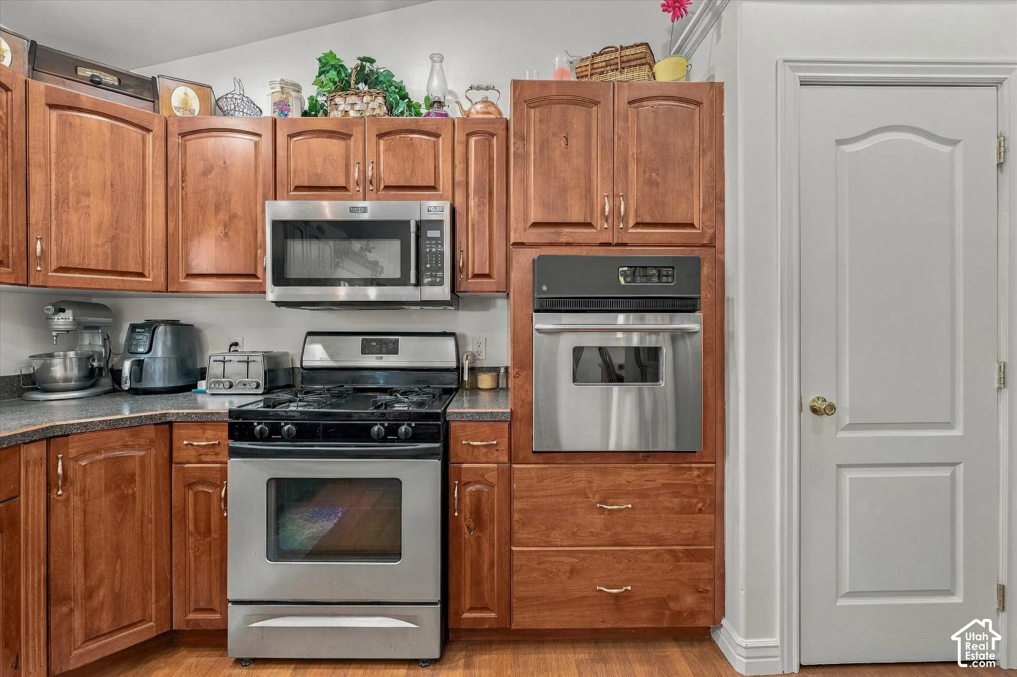 Kitchen featuring wood cabinetry, stainless steel gas range, over-the-range microwave, built-in wall oven, and dark-toned countertops