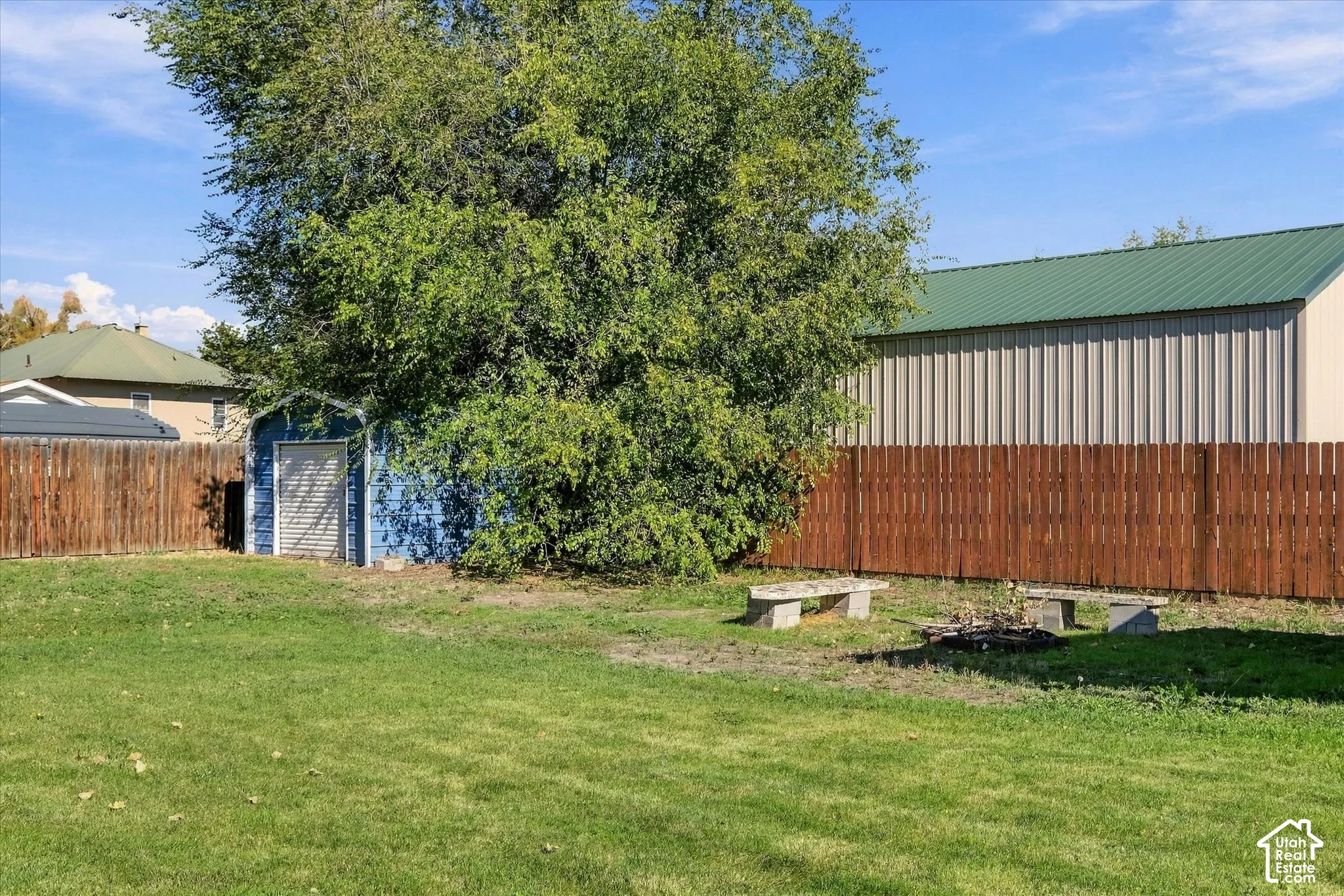 Backyard featuring a grass lawn, mature trees, wood privacy fencing, a metal-sided detached outbuilding, and a secondary storage shed