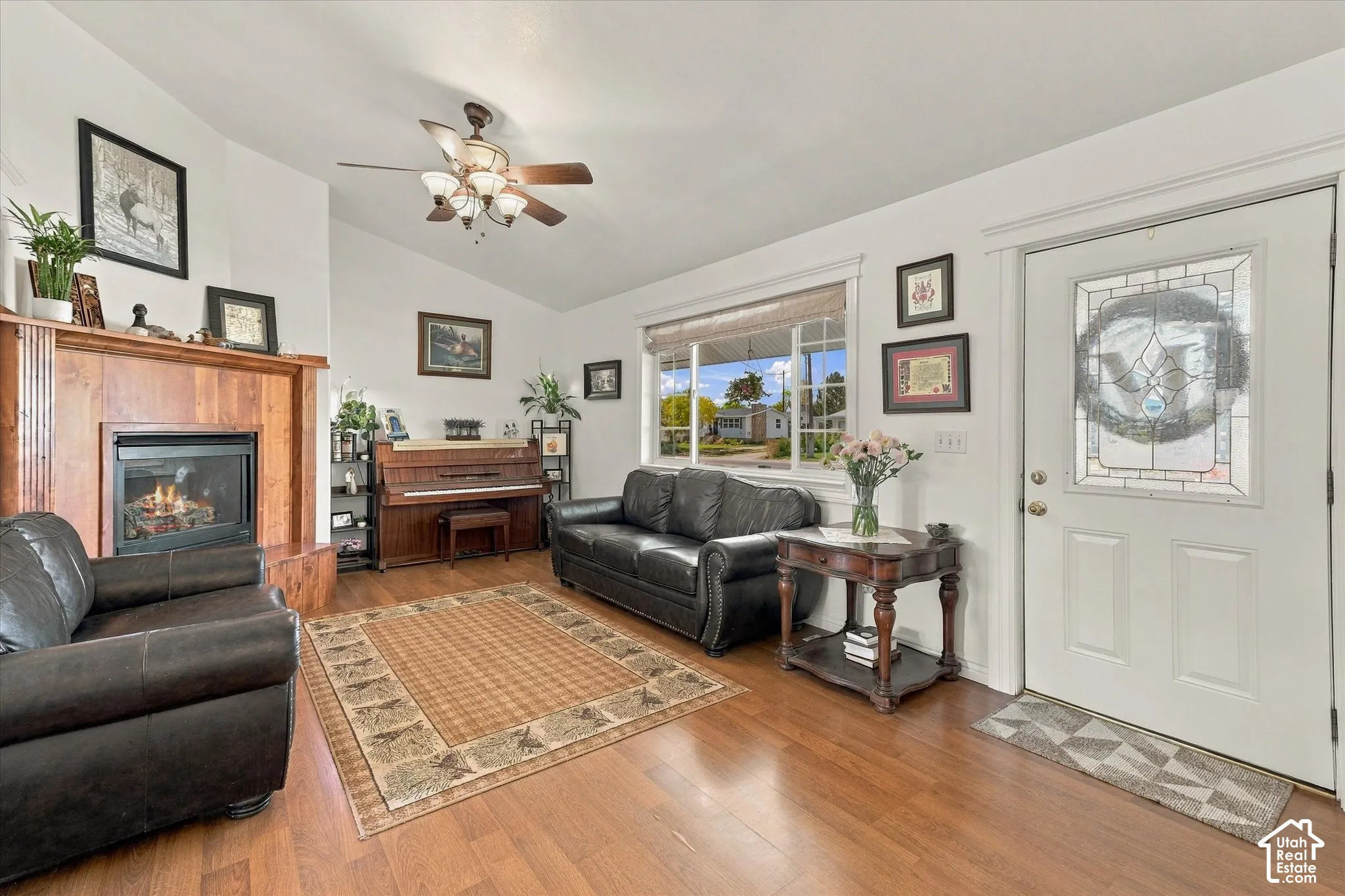 Wood-finish flooring, fireplace with a wood surround, vaulted ceiling with a central fan, and an entry door featuring a decorative glass insert