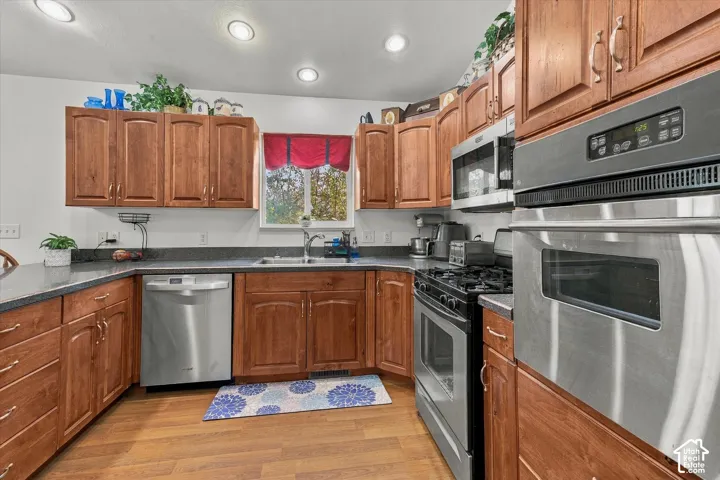 Kitchen featuring wood cabinetry, stainless steel appliances, dark countertops, recessed lighting, and a dual-basin sink