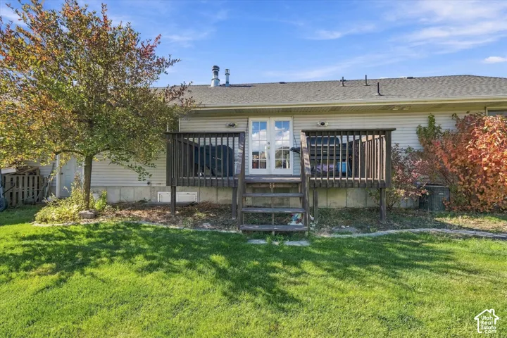 Rear exterior featuring a raised wood deck with stair access, light-toned horizontal siding, and glass-paneled double doors