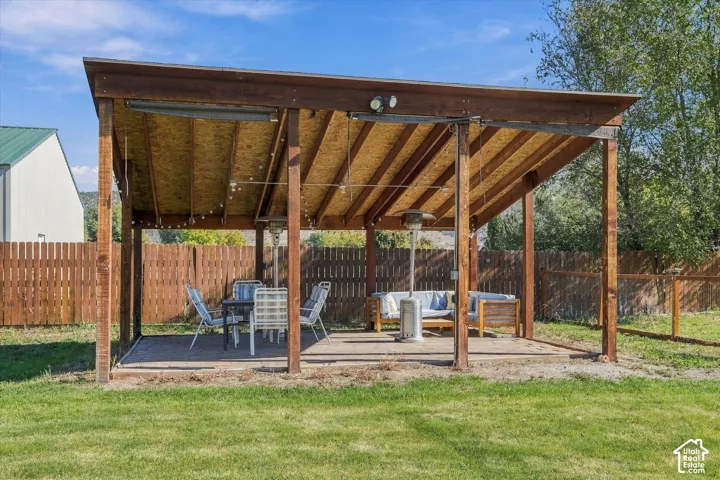 Covered outdoor patio featuring a timber-frame structure, exposed ceiling beams, concrete slab flooring, and perimeter wood privacy fencing