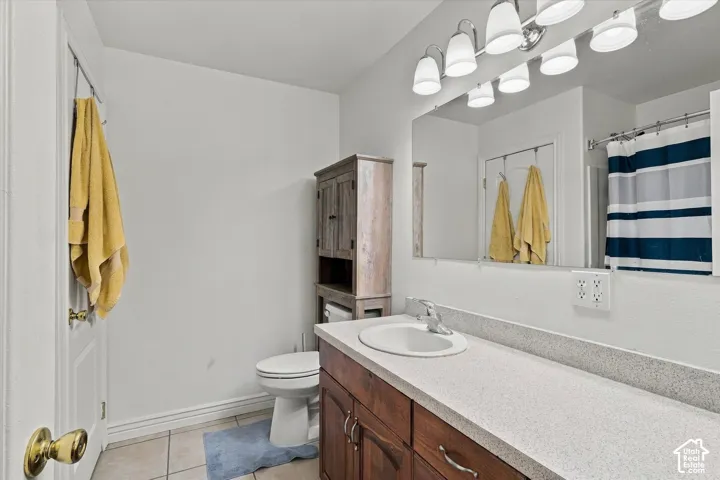 Bathroom featuring wood-finish cabinetry, a light-toned solid surface countertop, an undermount sink with a polished metal faucet, a large wall-mounted mirror, and multi-bulb vanity lighting