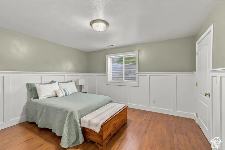 Interior room featuring wood-finish flooring, white wall paneling, a sliding window with egress well, and a flush-mount ceiling light fixture