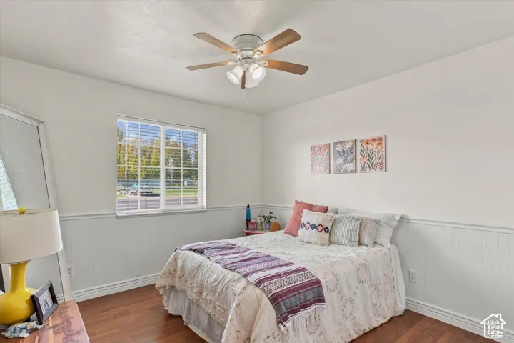 Interior space featuring wood-finish flooring, white beadboard wainscoting, a multi-pane window, and a ceiling fan with integrated light fixtures