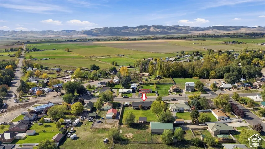 Aerial perspective featuring a single-story residence situated on a grass-covered lot, framed by expansive agricultural fields and a mountain range backdrop